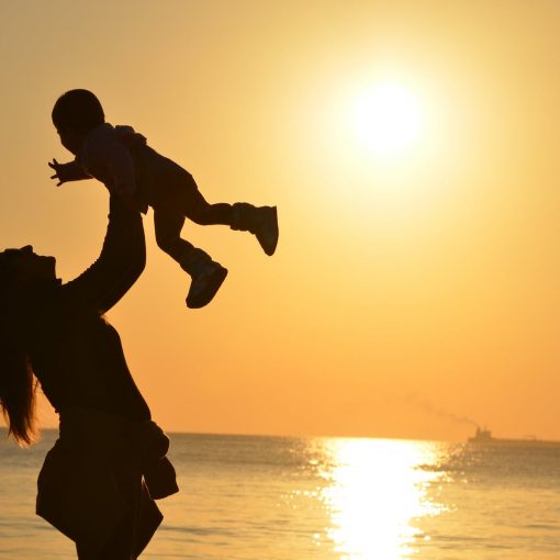 silhouette photo of a mother carrying her baby at beach during golden hour