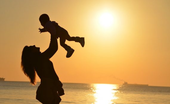 silhouette photo of a mother carrying her baby at beach during golden hour